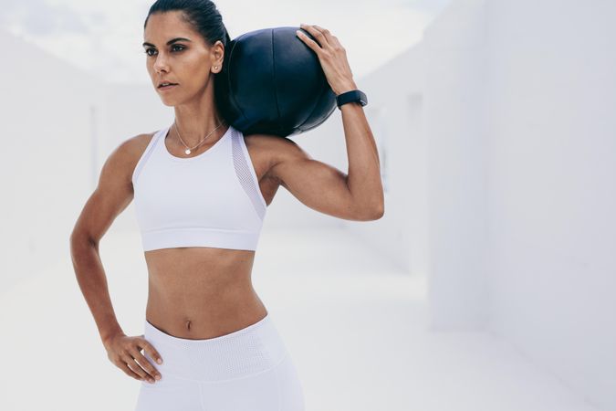 Athletic woman doing fitness workout holding a medicine ball on her shoulder