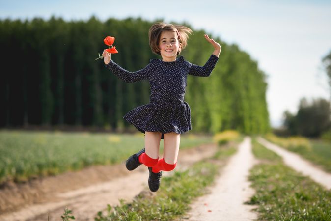 Happy girl jumping with red flowers in her hand