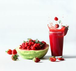 Splashing drink with watermelon served with red summer fruits, berries and red juice: strawberries and raspberries falling in glass