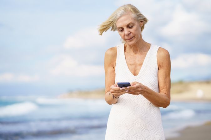 Mature woman using her smart phone on the beach, copy space