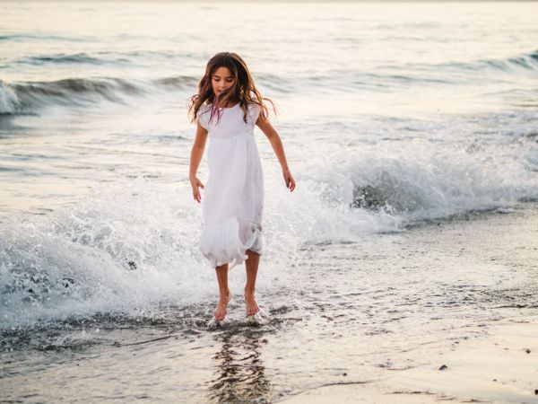 Adorable girl walking and playing on seaside at sunset
