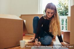 Woman sitting with packing boxes and making a list of items bxyaZ0