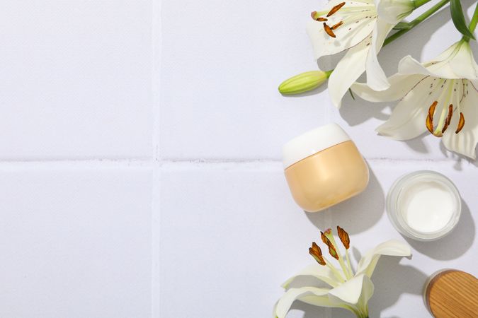 Jars with cream and lilies on light background, space for text