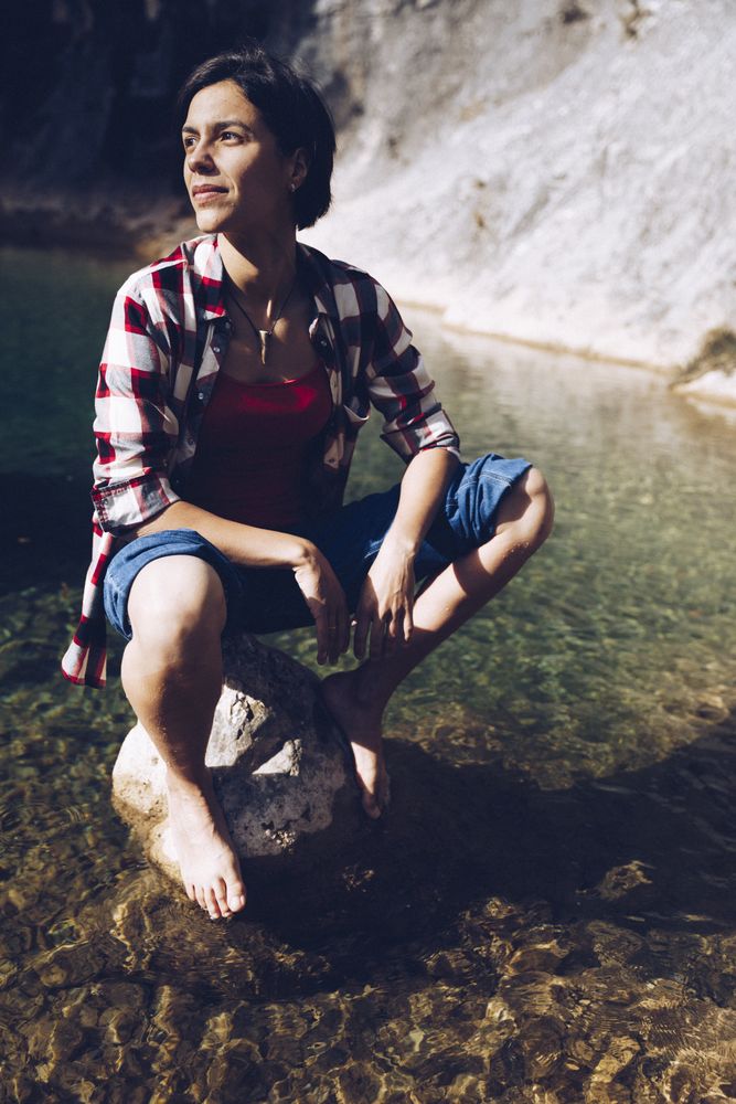 Cheerful woman sitting on rock in clear water