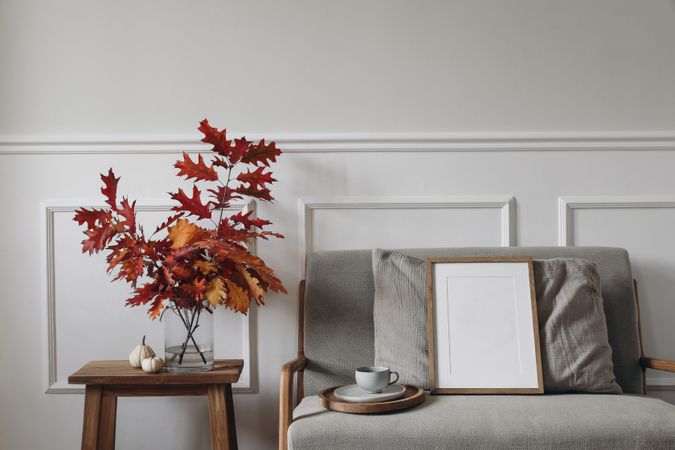 Red oak tree leaves, branches in vase in autumnal home with blank mockup poster