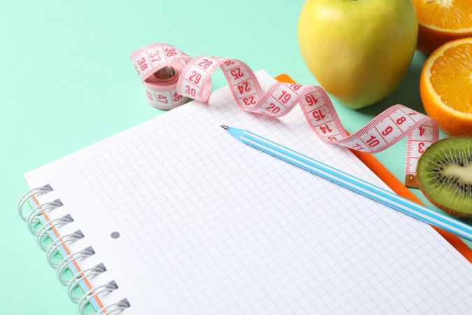 Notebook, measuring tape, pen and vegetarian food on mint background. Weight loss