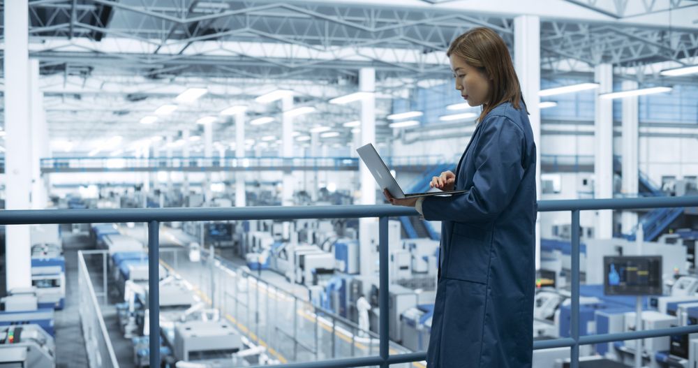 Portrait of a Japanese Engineer Using Laptop Computer and Looking Around a Factory Facility with Equipment Producing Modern Electronic Components for Different Industries