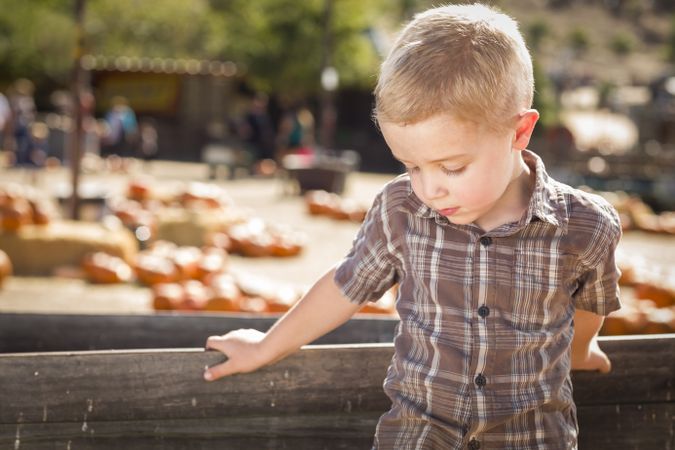 Sad Boy at Pumpkin Patch Farm Standing Against Wood Wagon.