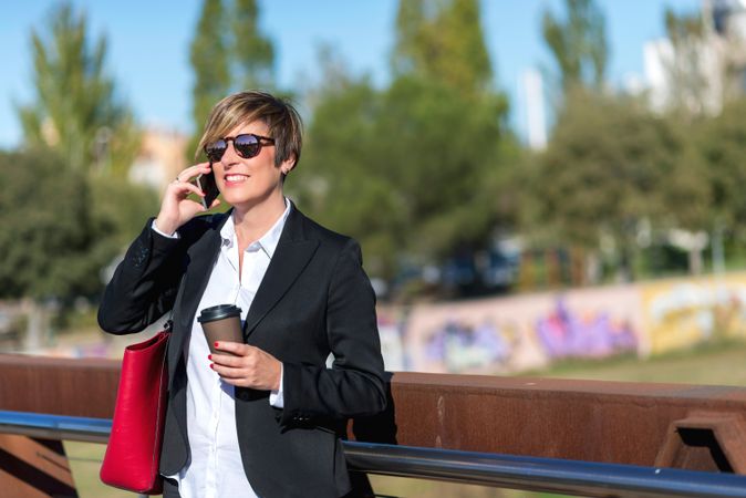 Businesswoman leaning on railing with coffee speaking on phone