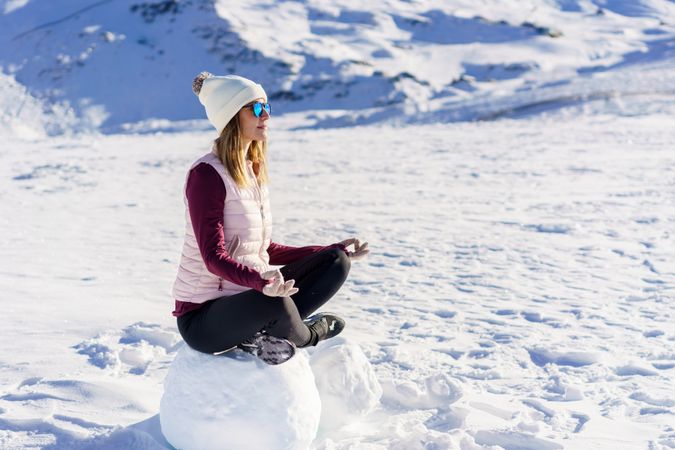 Side view of woman in snowsuit meditating on snowy mountain