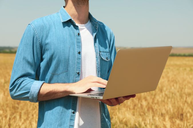 Young man with laptop in barley field. Agriculture business. Farming