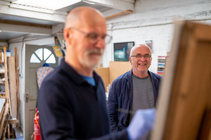 Male artist painting with smiling man behind him