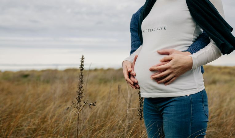 Pregnant woman with partner hugging and holding belly
