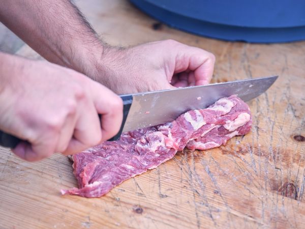 Crop male cutting pork with knife on wooden table