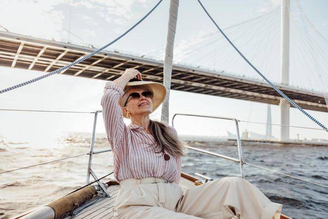 Stylish mature woman holding her hat on a yacht bow