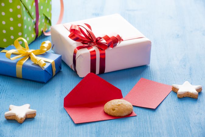 Three presents wrapped in colorful paper next to cookies on a blue table