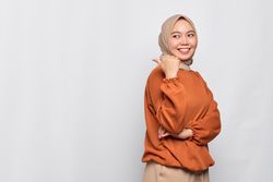 Smiling Muslim woman in headscarf and orange sweater pointing behind her with thumb and winking