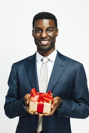 Image of smiling Black man presenting a gift wrapped in gold paper and red bow