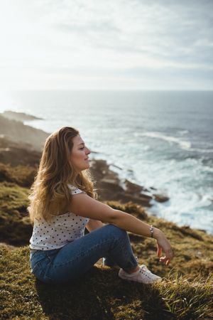 Pensive woman sitting on grass and looking at seascape