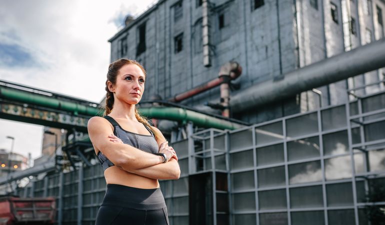 Sportswoman with crossed arms posing in front of a factory