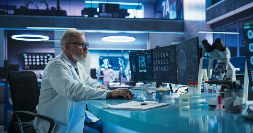 Male Neuroscientist Using Desktop Computer To Analyze MRI Scans Of Brain In Medical Research Center Laboratory.