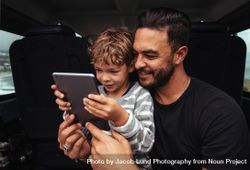 Young man and little boy using digital tablet while on road trip 0Lk1gb