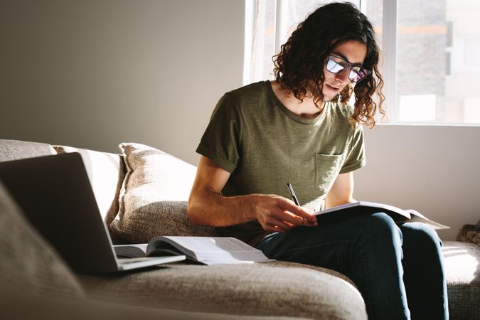 Student studying at home with books and laptop sitting on couch