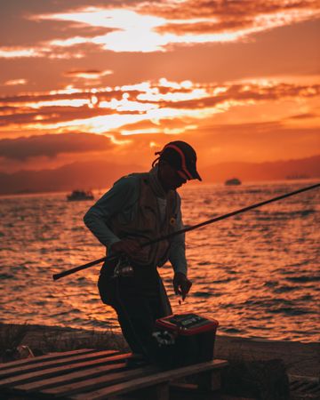 Man holding fishing rod standing on dock during golden hour