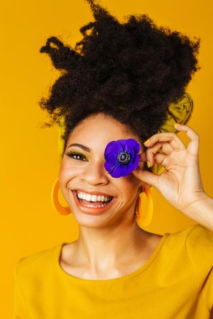 Smiling Black woman sticking her tongue out with one purple flower over her eye