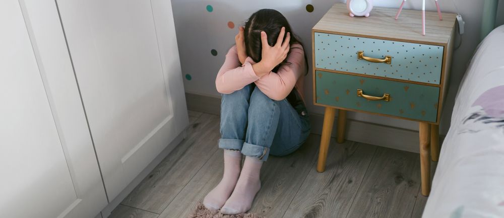 Unrecognizable girl with mental disorder holding head with hands sitting on the floor