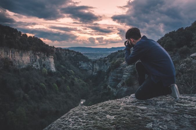 man with photo camera sitting on hill mountain with magnificent sunset