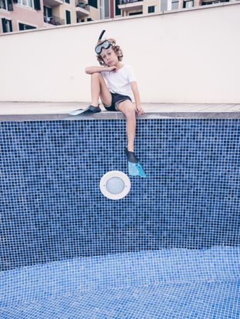 Puzzled boy in diving mask and flippers over empty pool