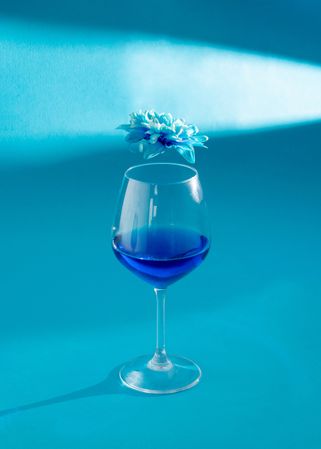 Wine glass with blue liquid and spring  flower above it