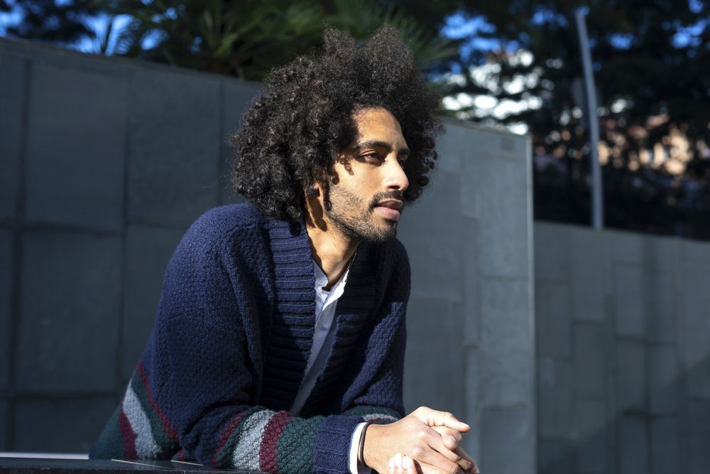 Portrait of handsome Black man in casual clothes, leaning forward outdoors on sunny day