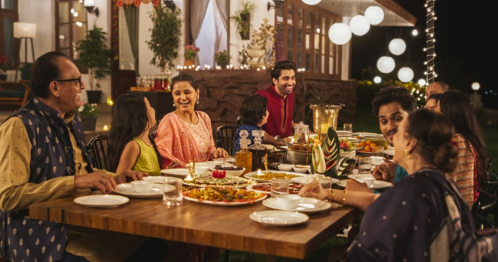 Happy Extended Indian Family Dining Together Outdoors in Fancy House Garden at Night.