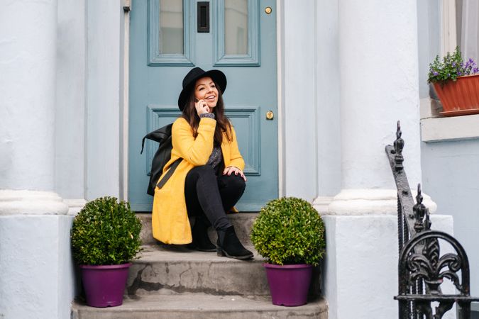 Happy female talking on smartphone on doorstep