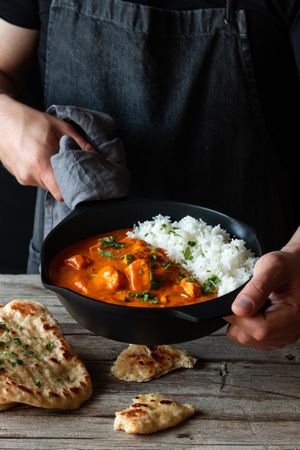 Faceless cook holding frying pan with hot butter chicken