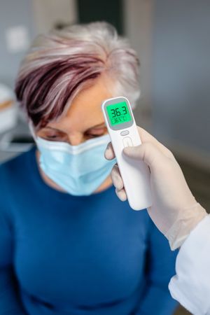 Mature woman with purple hues in hair without fever whose temperature is taken with an infrared thermometer