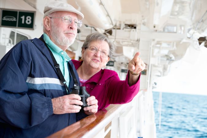 Mature Adult Couple Enjoying The View From Their Passenger Cruise Ship with Their Binoculars.