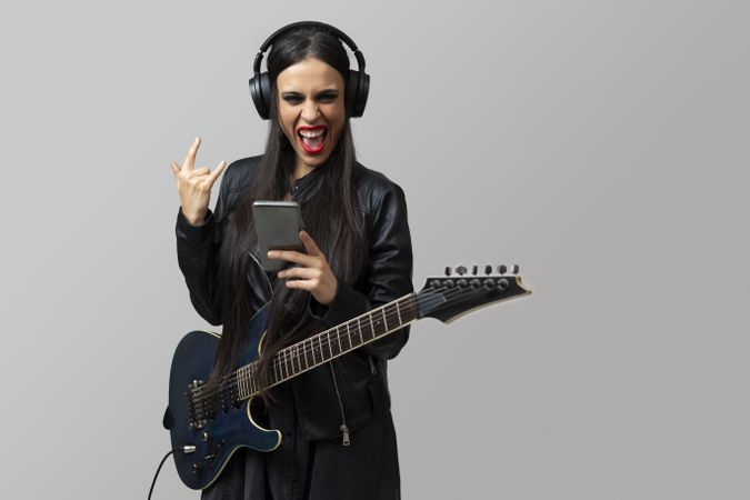 A young woman, guitarist, enjoys listening to music with the wireless headphones while make horns symbol with her hand