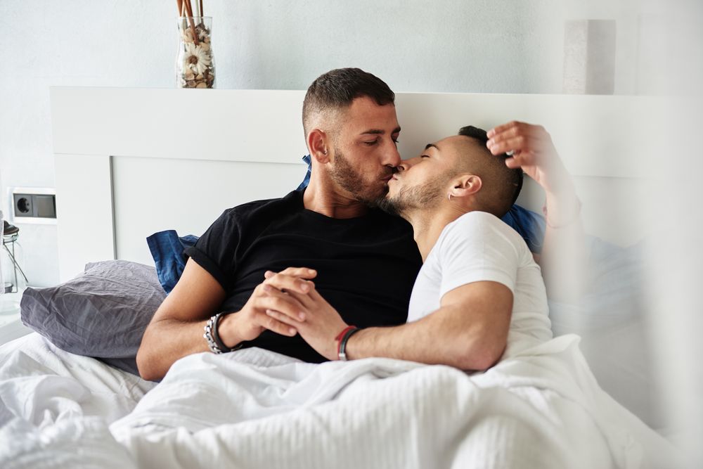Smiling gay couple hugging and kissing on bed