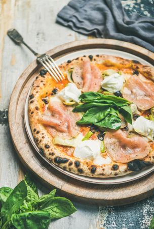 Freshly made wood fire oven pizza with spinach, ham and olives, on wooden background with linen