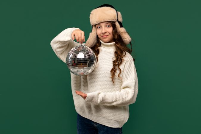 Girl in winter hat holding up disco ball playfully
