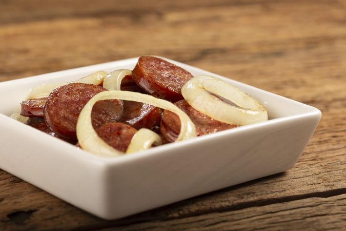 Sliced calabrese sausage with onion on wooden background.