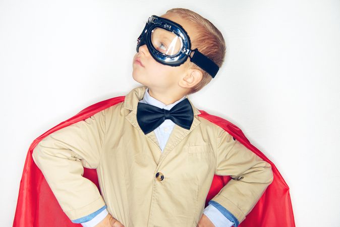 Serious blond boy looking away wearing airplane goggles and cape