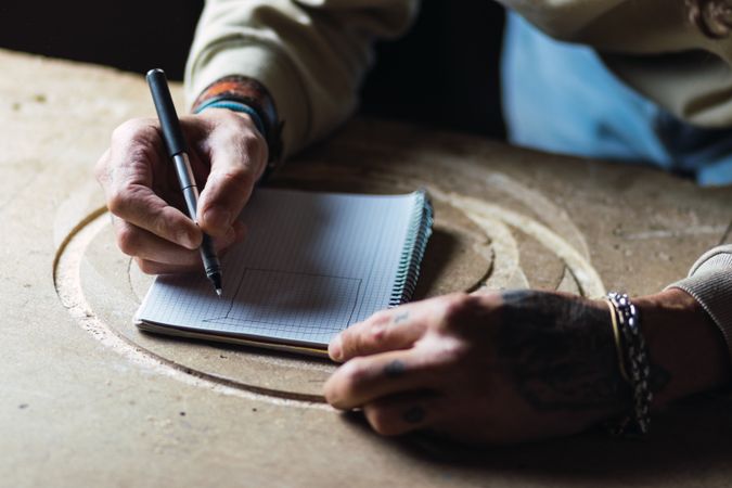 Crop woodworker drawing sketch in notebook