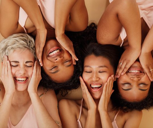 Happy females touching their faces while lying together on a beige background