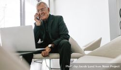 Mature businessman sitting in office lobby with a laptop using mobile phone 4d7jd5