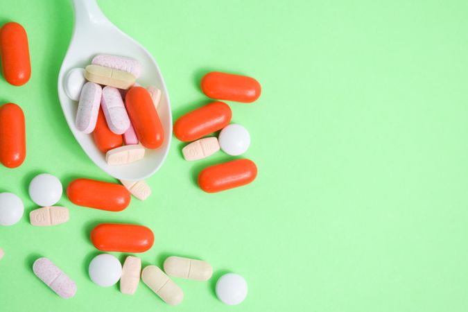 Top view of plastic spoon with pills and vitamins on green table