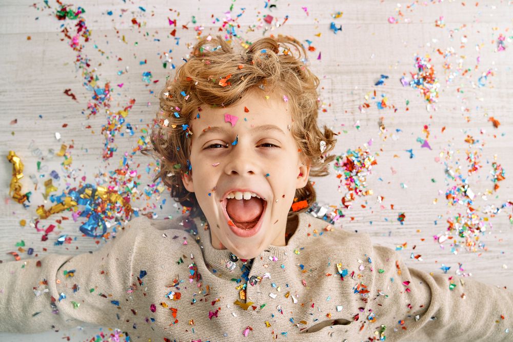 Excited little boy screaming joyfully covered with confetti